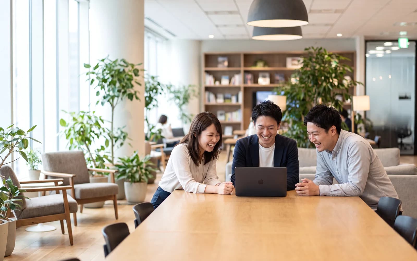 A hiring team laughing together around a laptop in a bright modern office