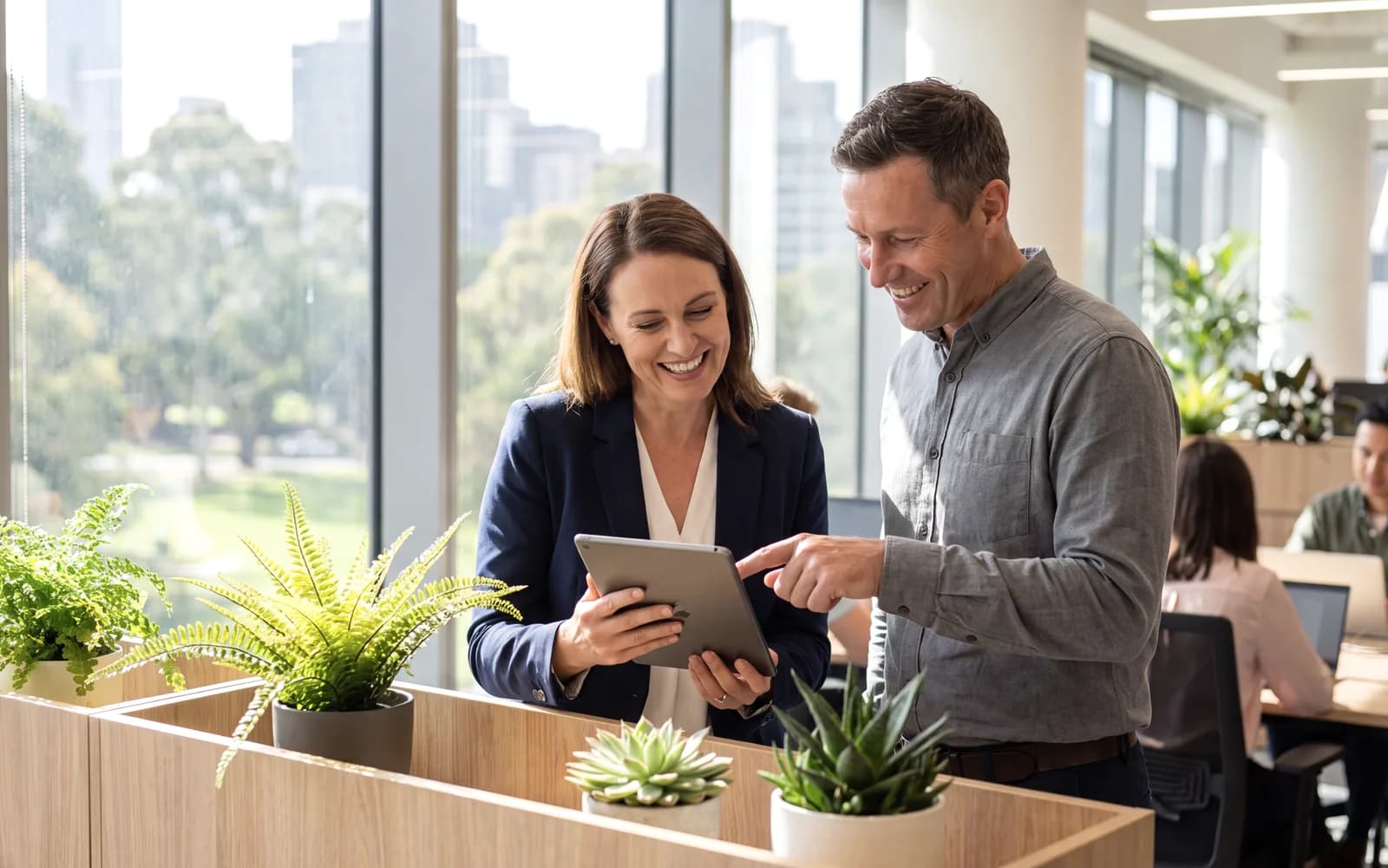 Two professionals standing in a meeting room reviewing a tablet together, one pointing at the screen